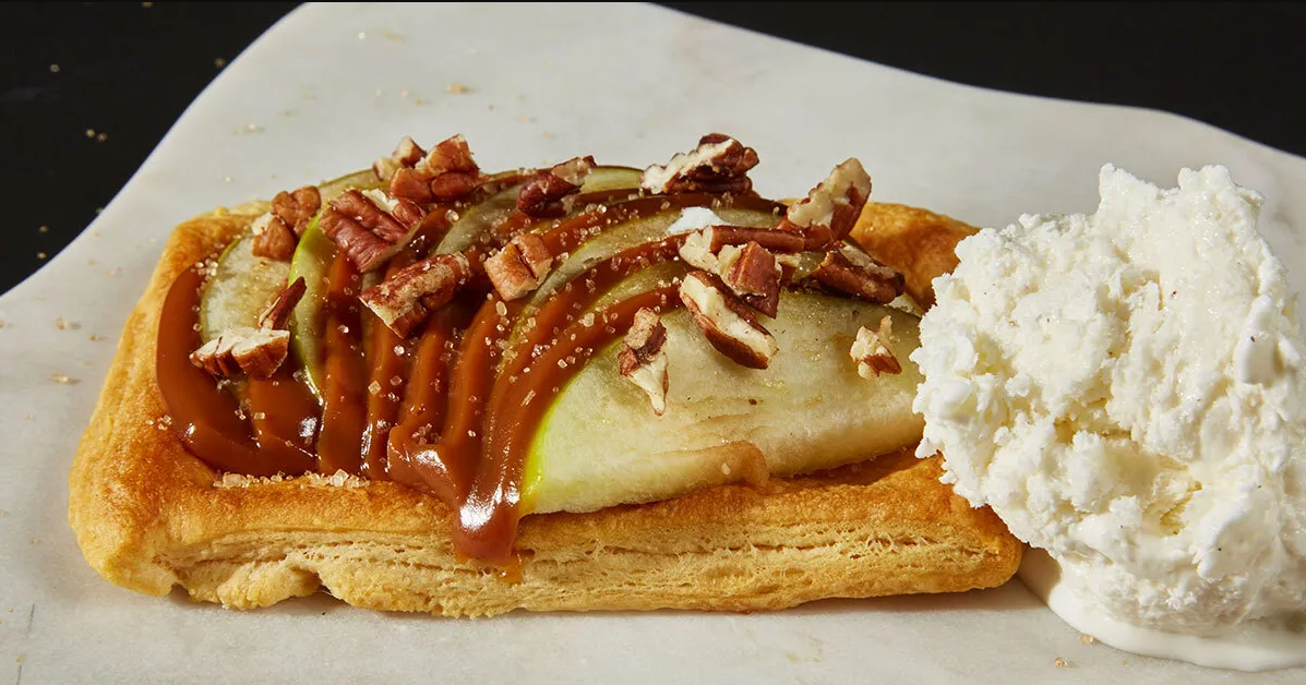 A Gertrude Hawk caramel dipped apple with chocolate and delicious toppings on a flaky tart with vanilla ice cream